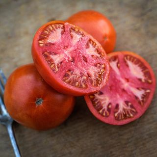 Close-up macro view of sliced and whole Peron Tomatoes on wooden cutting board.