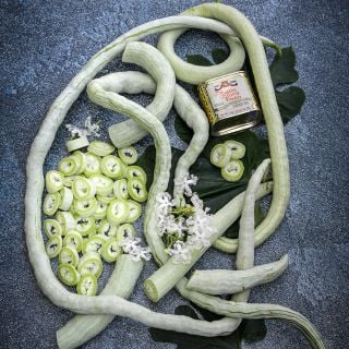 Whole and cut Indian Snake Bean with vintage curry powder can on a dark background.