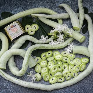 A closer view of whole and sliced Indian Snake Beans with fllowers all intertwined together.