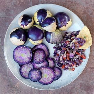 An overhead view of a plate of sliced and whole Purple Tomatillos with salsa and a corn chip.
