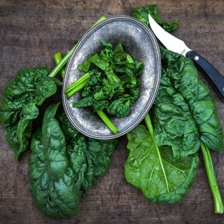 Giant Noble Spinach leaves with a knife on a wood board.   