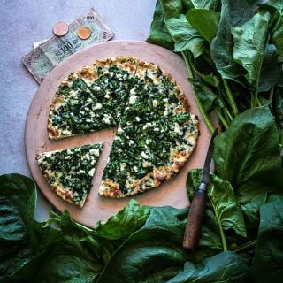 Gigante d' Inverno Spinach leaves surrounding a spinach and feta pizza on a pizza stone with Italian money.