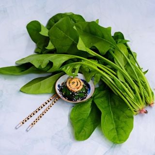 Jiromaru Spinach leaves with some cooked in bowl with chopsticks on light green background.