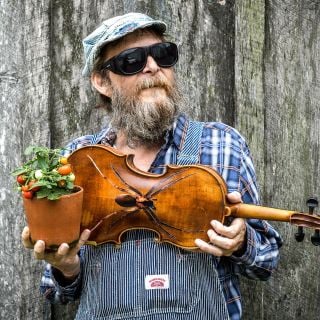 A musician poses with amini-tomato and his fiddle with a "fiddler spider" at the Baker Creek Spring Planting Festival.