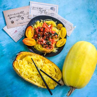 Whole raw and cooked Kinshi Noodle Winter Squash with Japanese postcards on a blue background.
