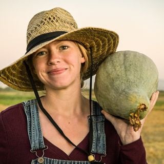 Baker Creek Manager holding a Sibley or Pikes Peak Winter Squash on her shoulder in the field.