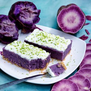 Sweet cakes on a plate made from Lilac Beauty Sweet Potatoes surroundded by potatoes on a blue background.