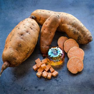 Whole and cut Pumpkin Yam Sweet Potatoes with a glass pumpkin on a brown background.