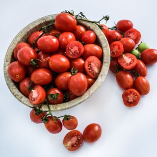 A bowl full of  A Grappoli D'Inverno Tomatoes surrouunded by cut tomatoes on a white background.