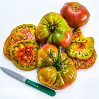 Whole and cut Ananas Noire or Black Pineapple Tomatoes with a green handled knife on a white background.