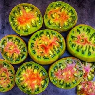 Overhead view of sliced Ananas Noire or Black Pineapple Tomatoes on dark brown background.