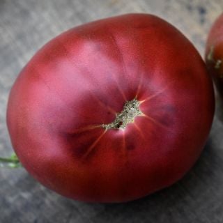 A close-up of a single Black from Tula Tomato, showing its deep rich color, on a wood background.