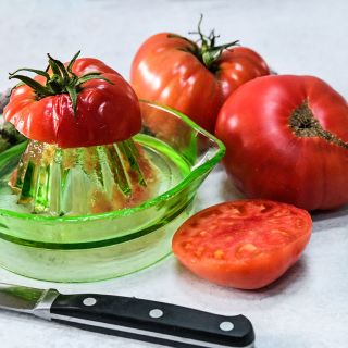Sliced and whole Brandywine Sudduth's Strain Tomatoes with a hand juicer and tomato juice.