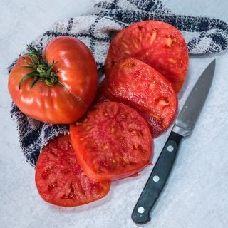 A Brandywine Sudduth's Strain Tomato with four slices on dish towel with a knife.