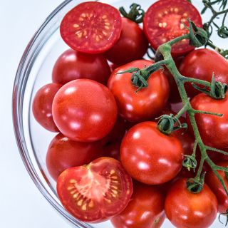 Close-up view of Chadwick Cherry or Camp Joy Tomatoes in a glass bowl on a white background.