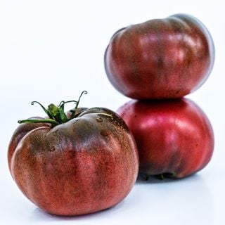 A trio of Cherokee Purple Tomatoes on a white background.