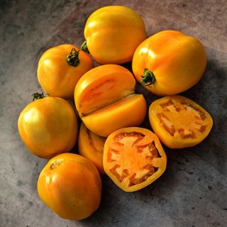 Cut and whole Dad's Sunset Tomatoes on a brown background.