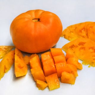 A whole Dr. Wyche's Yellow Tomato surrounded by cut and sliced tomatoes.
