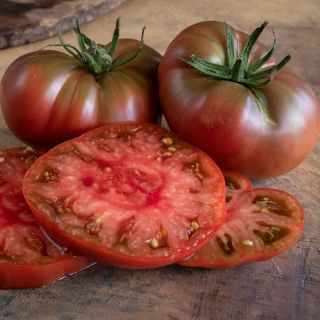 A couple of whole True Beefsteak or Fejee Improved Tomatoes with slices on a brown background.