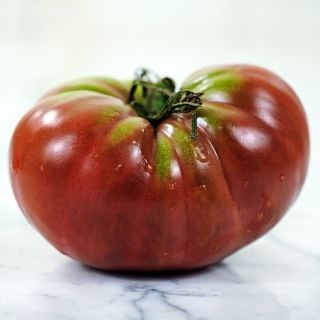 A side view of a single True Beefsteak or Fejee Improved Tomato on white marble countertop.
