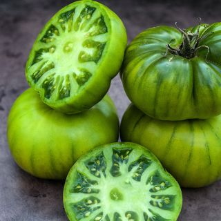 Cut and whole Grandma Oliver's Green Tomatoes on a brown background.