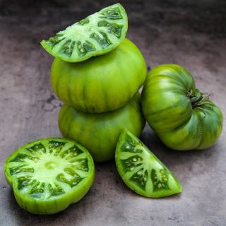 Sliced, sectioned and whole  Grandma Oliver's Green Tomatoes stacked up on a brown background.