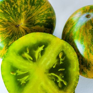 Macro close-up of whole and cut Green Zebra Tomatoes on light background.