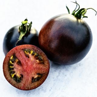 A trio of Indigo Blue Chocolate Tomatoes with one sliced in half to show the red meat inside.