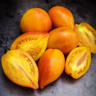 Cut and whole Marina's Praise Tomatoes on a dark brown background.