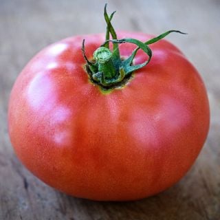A close-up of a single Ozark Pink Tomato on wood.