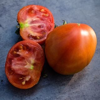 Close-up view of whole and halved Pantano Romanesco Tomatoes on a dark brown rustic background.