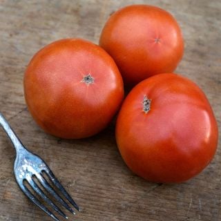 Three whole Peron Tomatoes with an old tarnished fork on wood cutting board.
