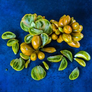 Phil's Two Tomatoes sliced and whole arranged on a deep blue background.