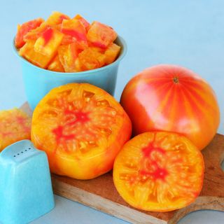 Cut, sliced and whole Pineapple Tomatoes on a wooden cutting board with a light blue background.