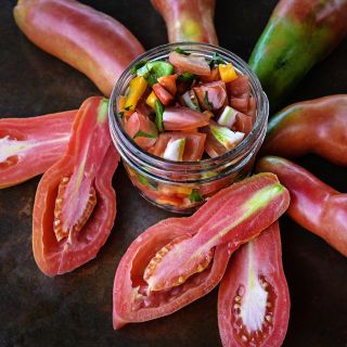 Close-up of cut and whole Pink Fang Tomatoes with salsa in a jar on a copper background.