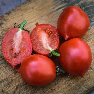 Close-up of cut and whole Principe Borghese Tomatoes on a wooden cutting board.