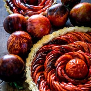 A tomato tart with Queen of the Night Tomatoes surrounding the tart on wooden cutting board.