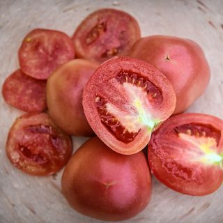 Cut and whole Raspberry Lyanna Tomatoes on a pink terra-cotta plate.