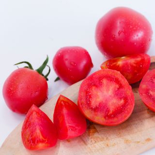 Close-up of Raspberry Lyanna Tomatoes on wood cutting board and white background.