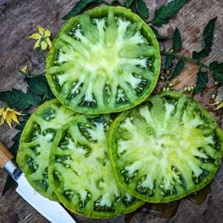 Four giant slices of Aunt Ruby's German Green Tomato on a cutting board with a knife and blooms.