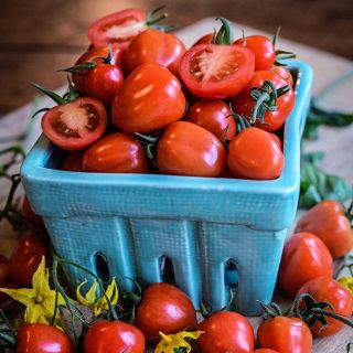 Sweetheart Cherry Tomatoes in aberry container with blooms on a wood background.