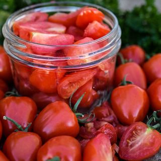 Close-up view of whole and cut Sweetheart Cherry Tomatoes with some in a canning jar.