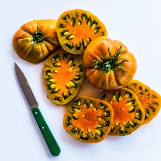 Sliced and whole Thorburn's Terra-Cotta Tomatoes with a dark green handled knife on white background.