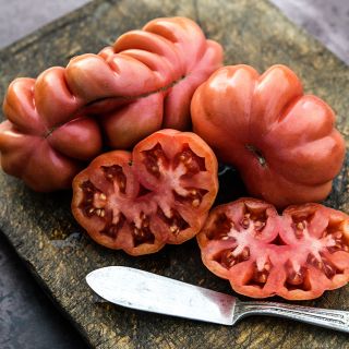 Fully ripe Tlacolula Pink Tomatoes, sliced and whole, on a wooden cutting board with a knife.