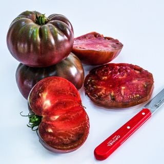 Cut and whole True Black Brandywine Tomatoes on a white background.