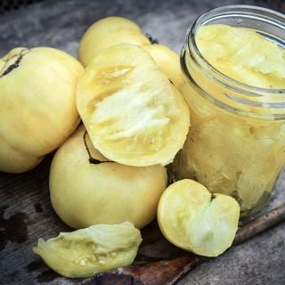 Cut and whole White Tomesol Tomatoes one a wooden cutting board with some cut in a mason jar.