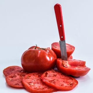 A whole Wood's Famous Brimmer Tmato surrounded by slices with a knife on white background.