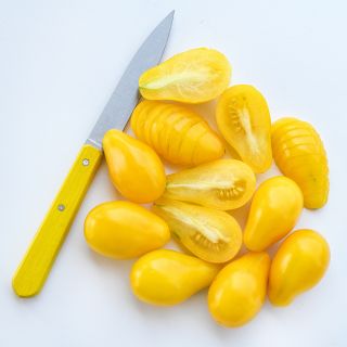 Sliced and whole Yellow Pear Tomatoes arranged on white background with a yellow handled knife.