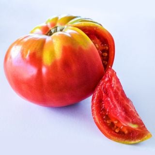 A single Brandywine Sudduth's Strain Tomato with a slice removed on a white background.