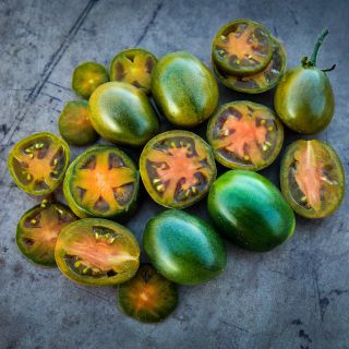 Cut and whole Evil Olive Tomatoes arranged in a pleasant display on brown rustic background.